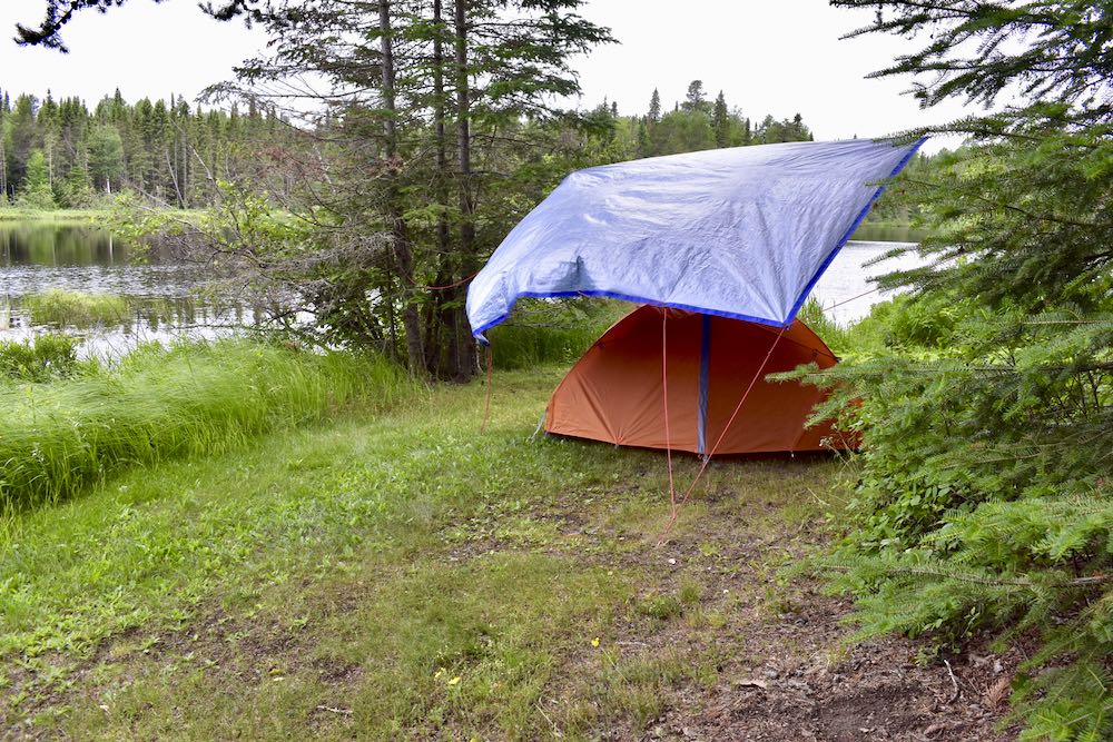 orange tent with blue tarp at lakeside campsite