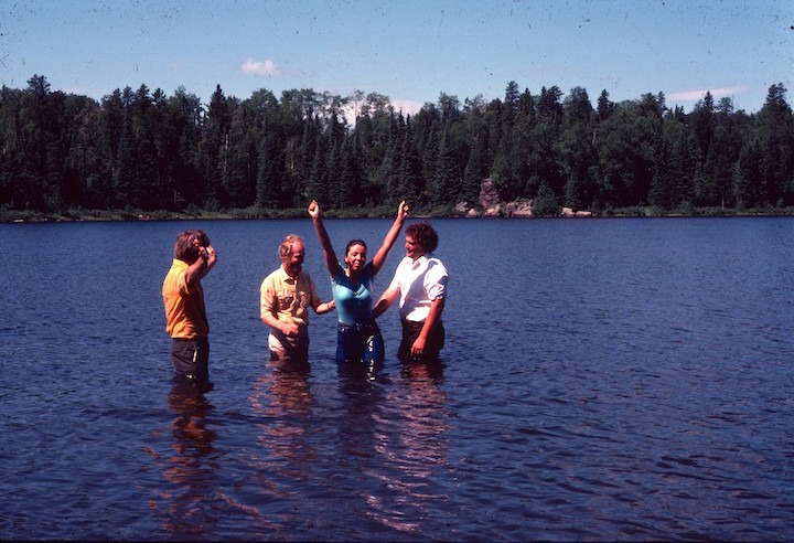 two men baptizing a woman in Bow Lake while another man looks on