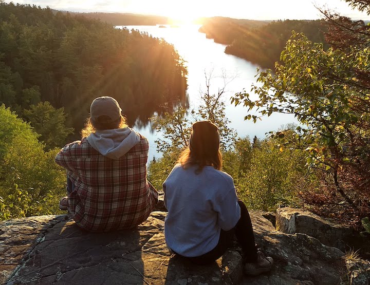 two women sitting on a rock overlooking Bearskin Lake at sunrise