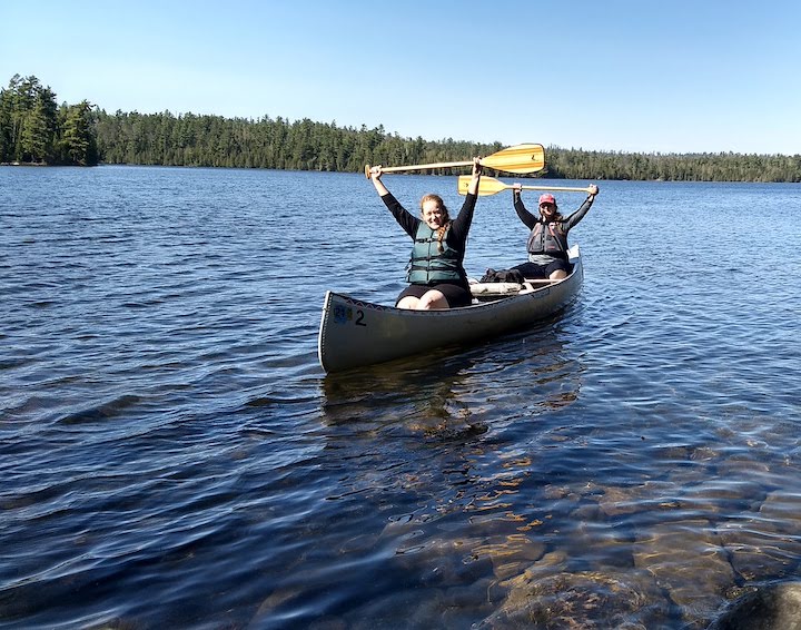 two women in a canoe with their paddles raised over their heads