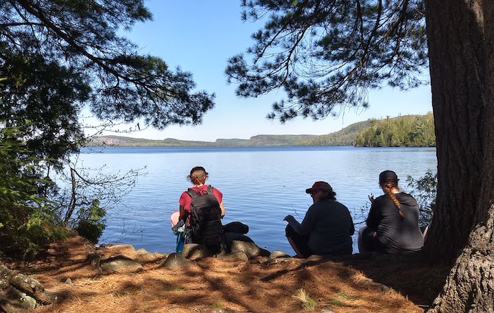 three women relax along a lake shore