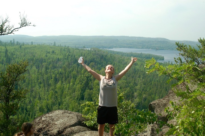 woman with arms raised on High Cliffs overlook at Gunflint Lake