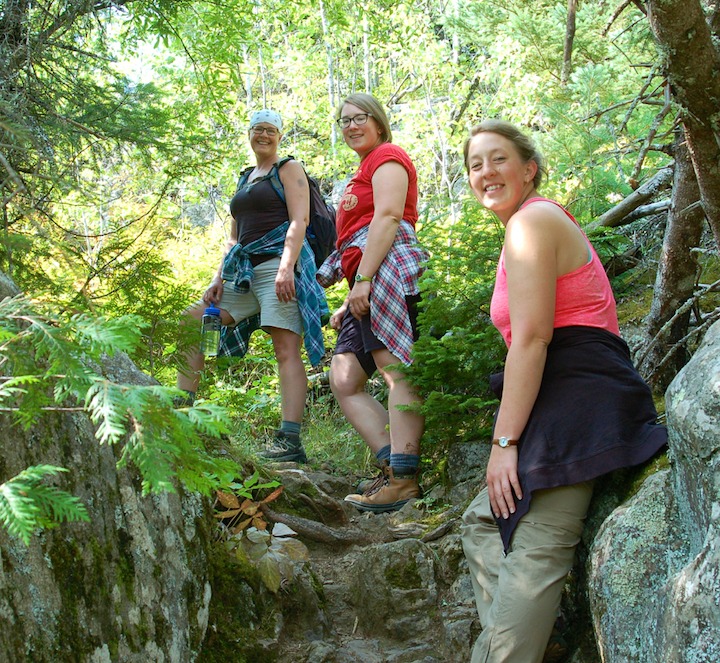 three women hike uphill in the woods