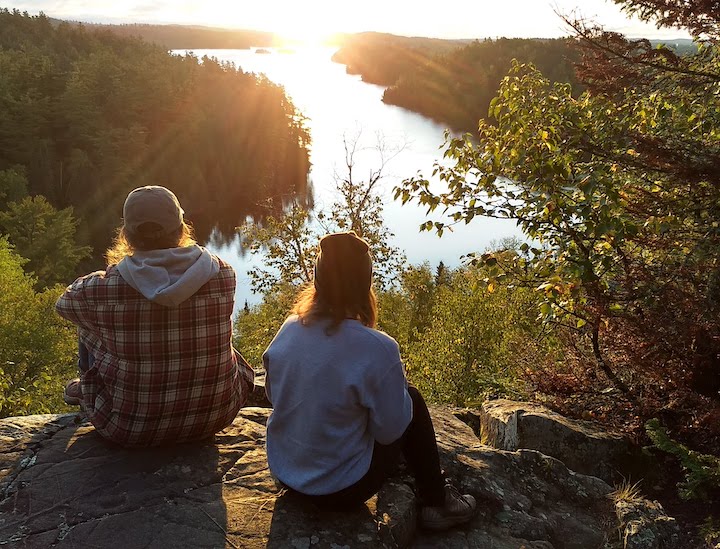 two women sit on Caribou Rock watching the sun rise over West Bearskin Lake