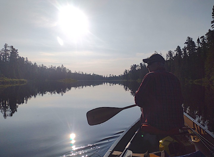 man sitting in the bow of a canoe on a glassy lake 