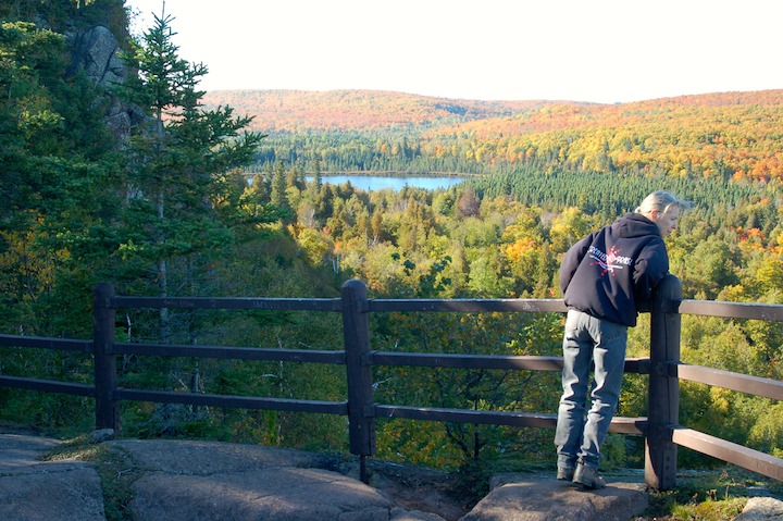 woman looks over railing at an overlook on Oberg Mountain; Oberg Lake in the distance, fall