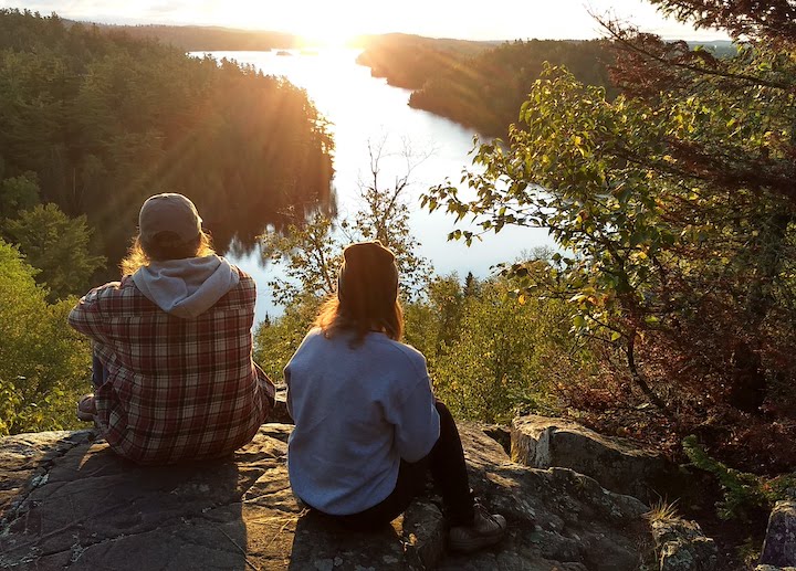 two women sit on Caribou Rock, watching the sun rise over Bearskin Lake