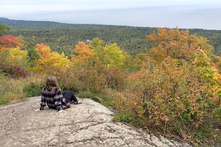 woman sits on a rock high above Lake Superior on the Oberg Mt trail