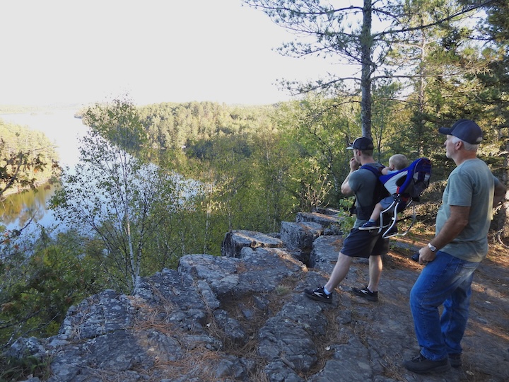 dad with his toddler in a packpack and grandpa looking over Caribou Lake on a hike