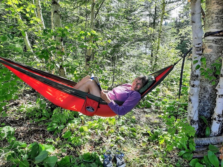 woman reads in a red hammock at her campsite