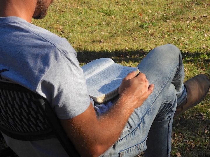 man sits outside reading his Bible