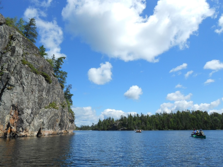 people in two canoes paddle by high cliffs on Seagull Lake