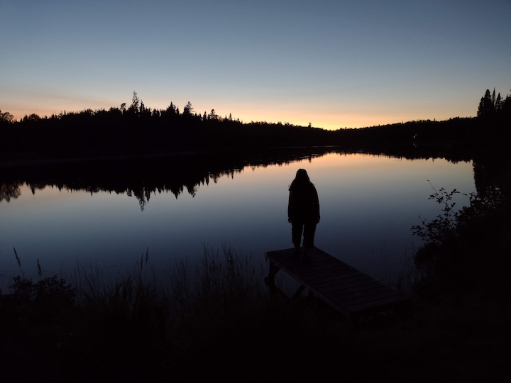 woman stands on a dock at a lake at dusk