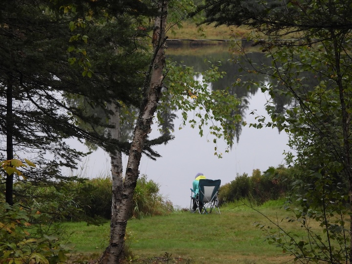 camper sits in a camp chair next to Bow Lake at Okontoe Family Campground