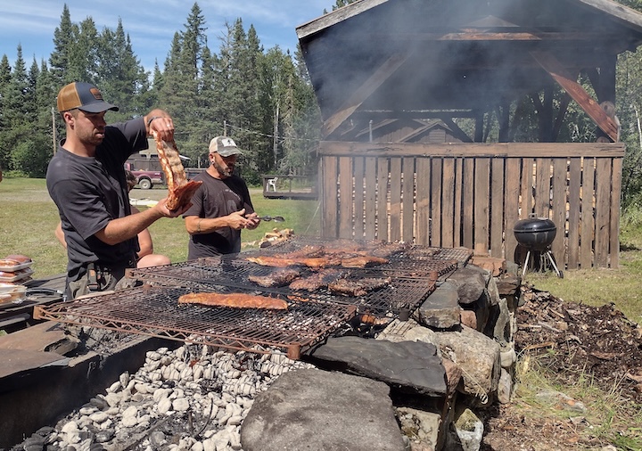two men put racks of ribs on a big stone grill