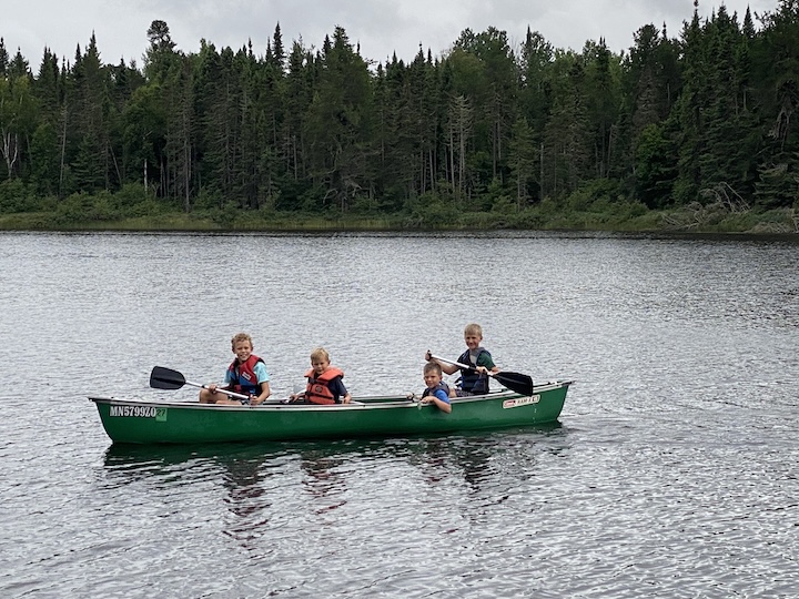 four young boys in one canoe paddle on Bow Lake at Okontoe