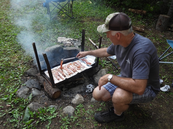 man cooks bacon on a grate over a campfire