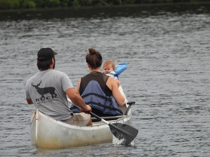 a husband, wife and baby in a canoe on a calm lake