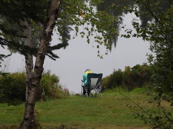 camper sits in a camp chair next to the lake
