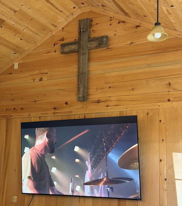 The wood cross that hangs in front of the Okontoe Chapel, above the tv screen