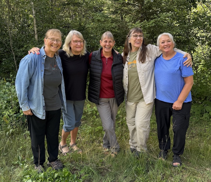 five women stand together in front of the trees